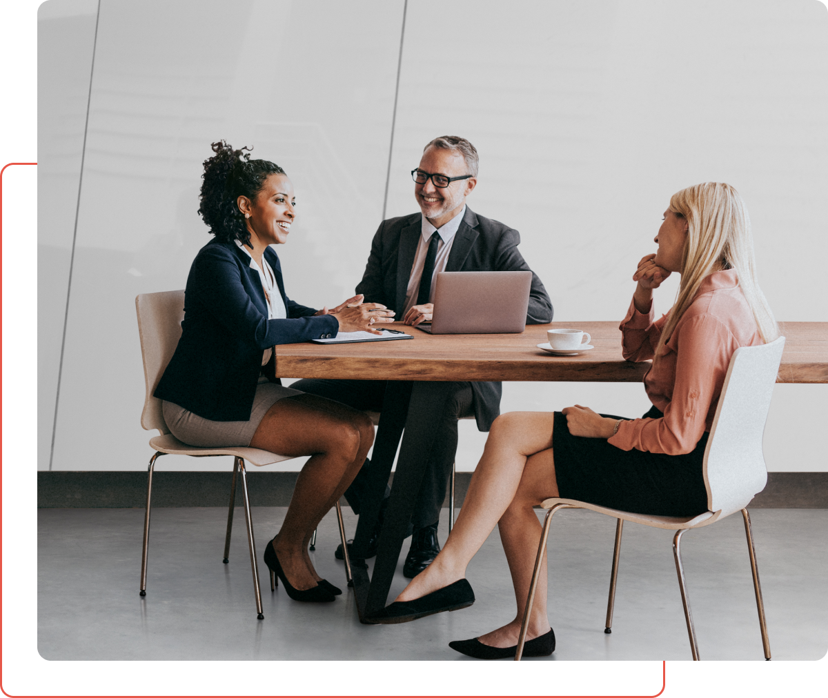 Three people sitting at a table with one of them looking at the other person on his laptop.